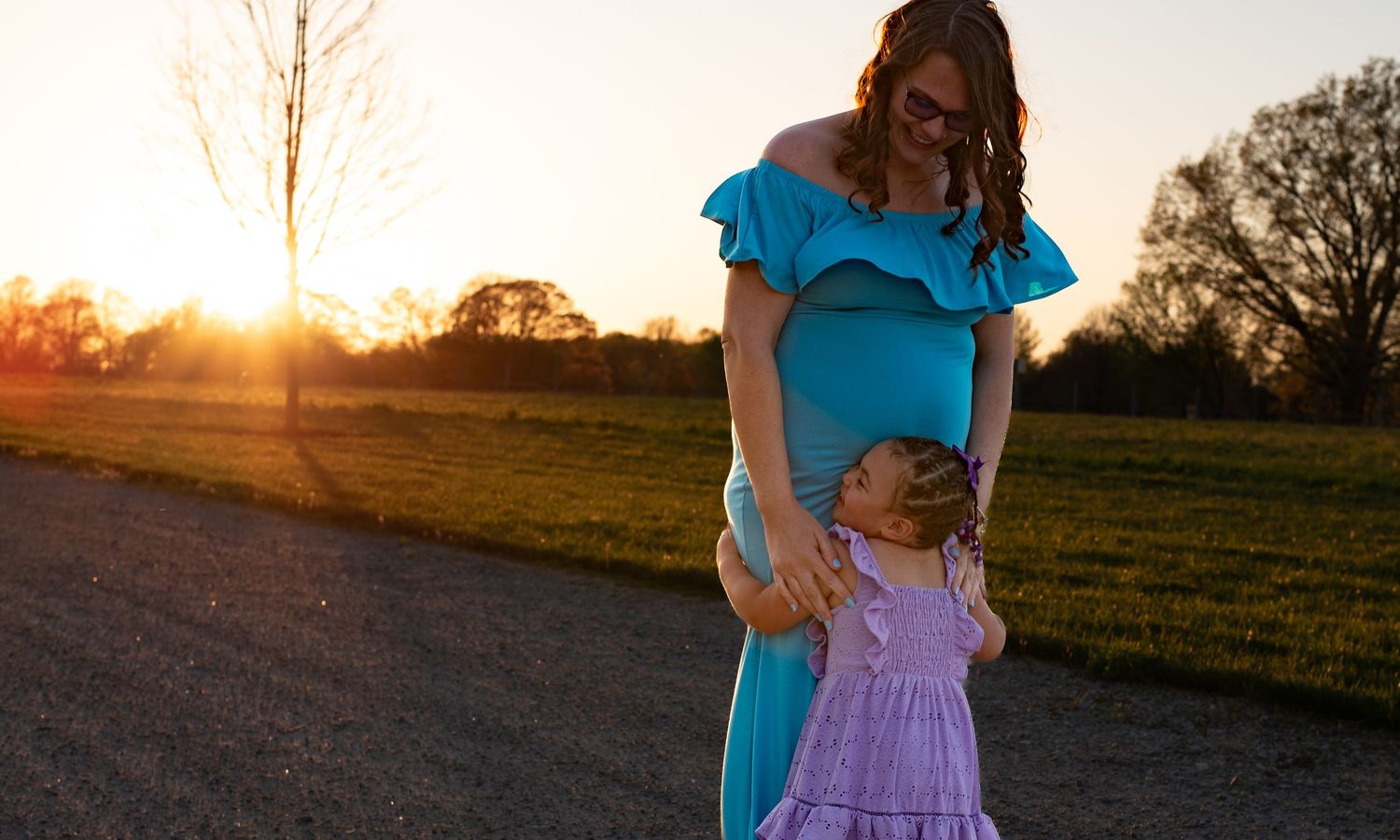 A sunset portrait of two people in blue and purple dresses walking on a country road.