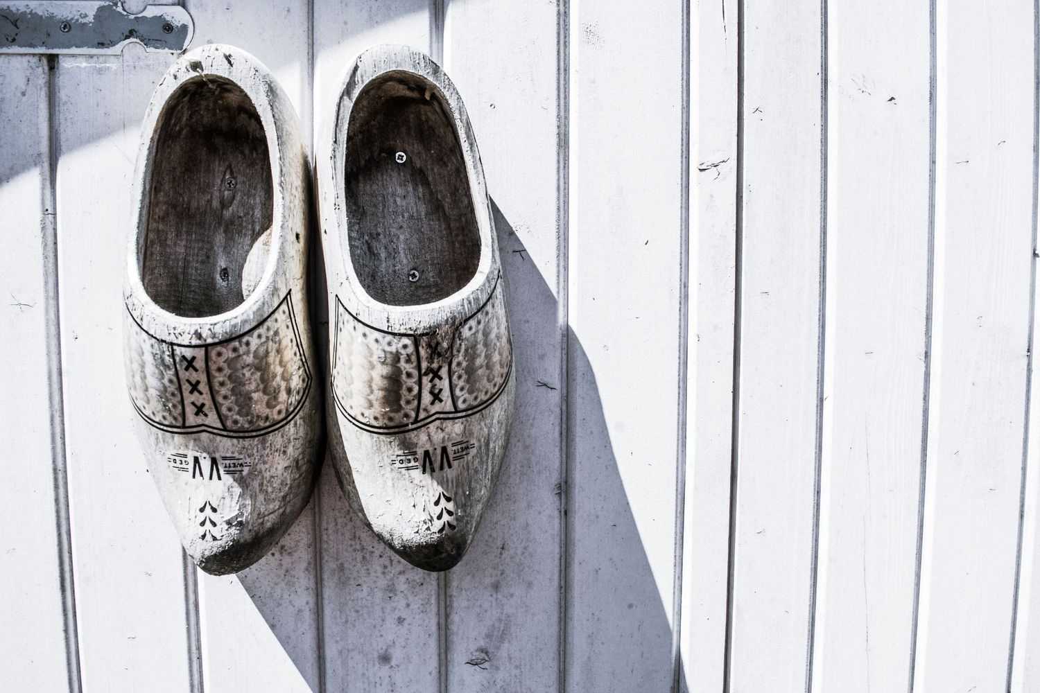 Pair of weathered white wooden clogs casting shadows on a white wall.