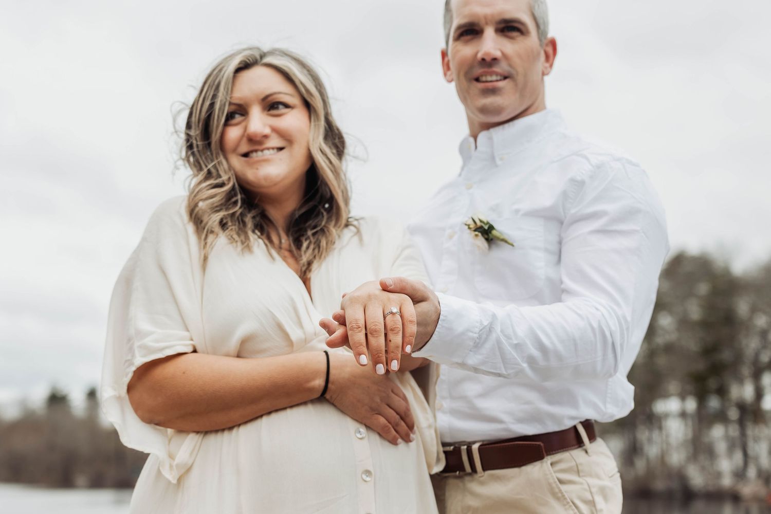 A couple shows off their engagement ring while posing outdoors.