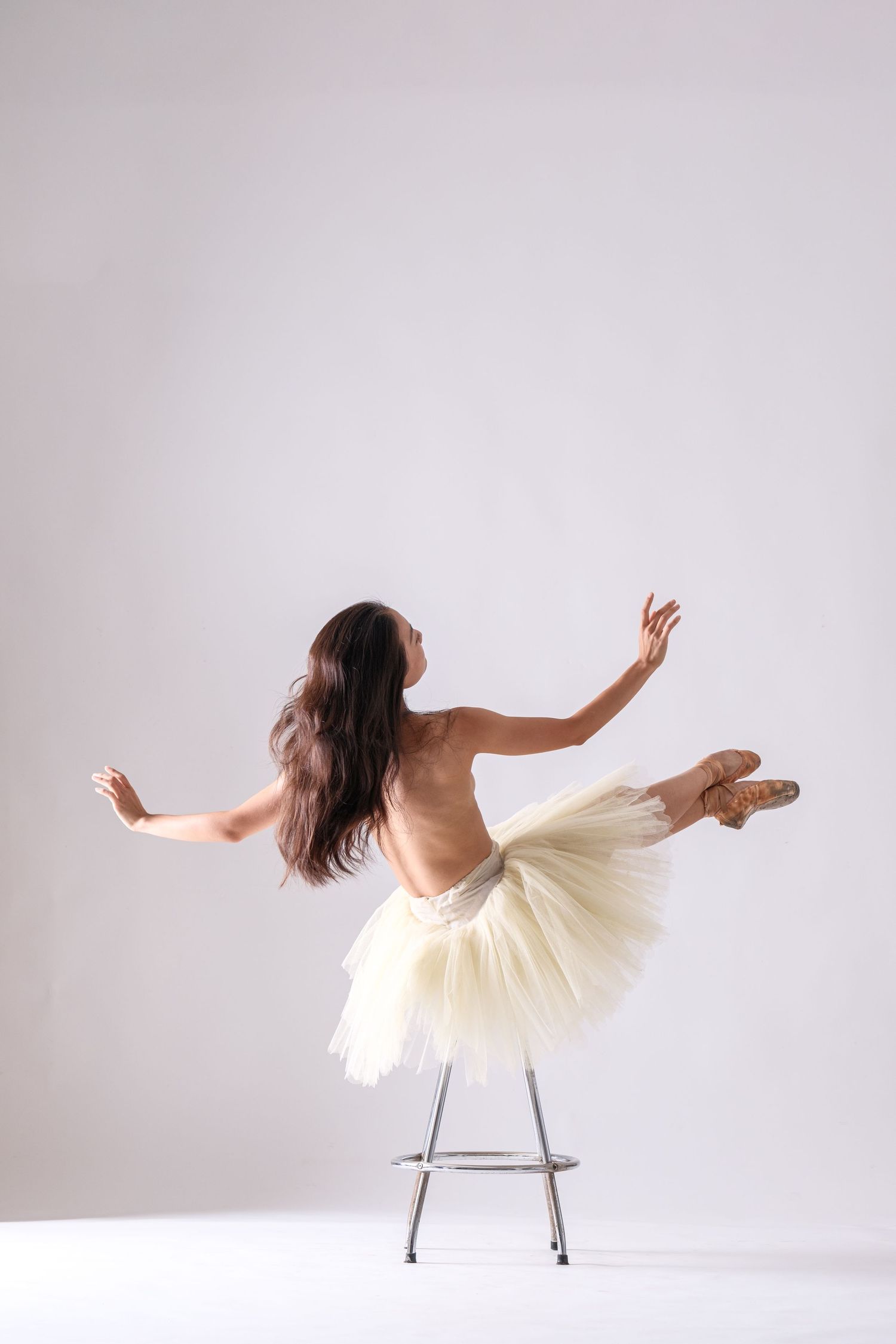 Artistic photo series of a dancer in a tutu reclining on a white chair against light background.