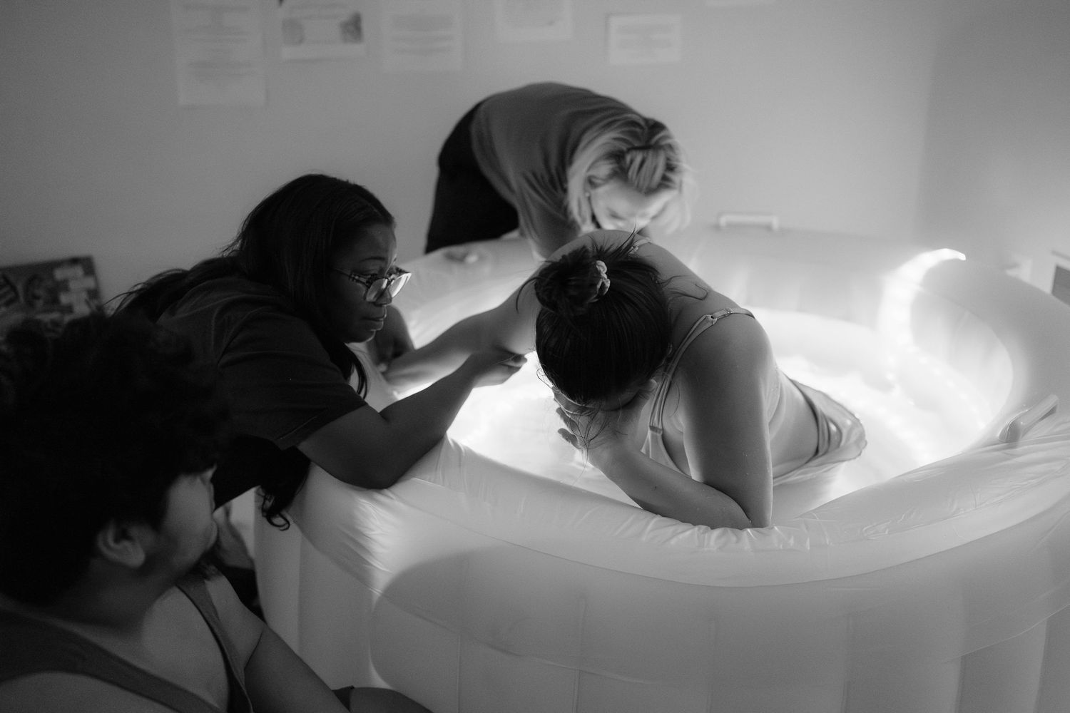 A midwife assists a pregnant woman positioned in a birthing tub during labor to give birth at home in Frederick, MD