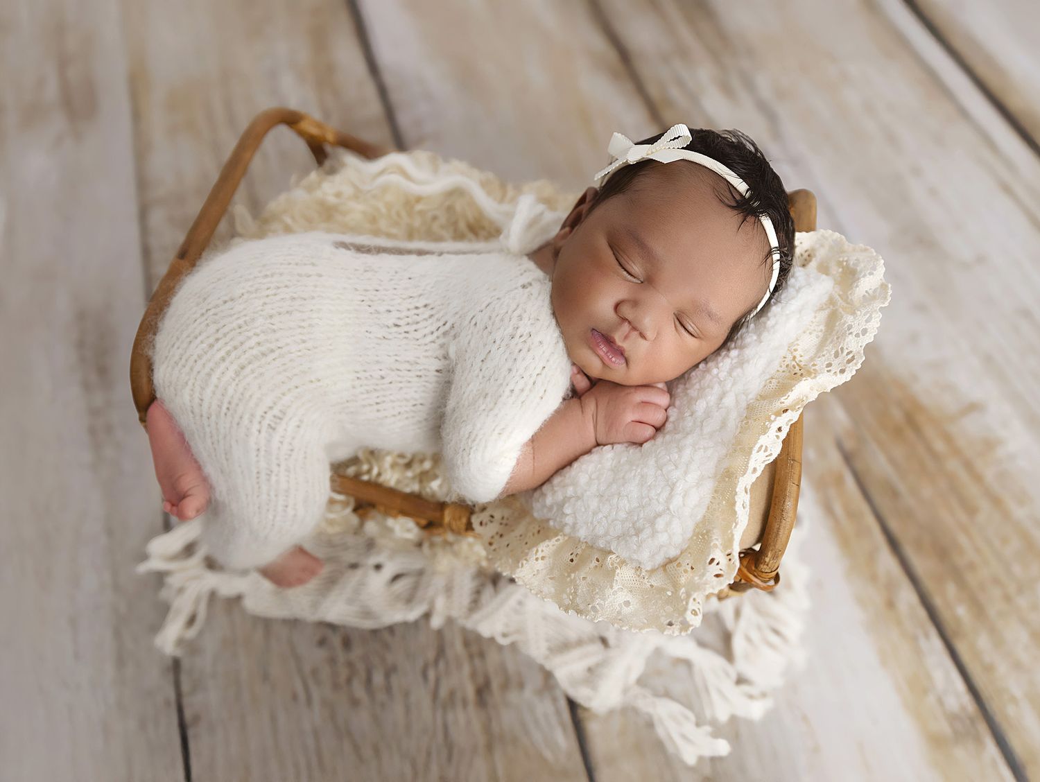 Image of a beautiful newborn baby girl dressed in a white fluffy romper laying on a little cane pine bed taken in my home studio in Coventry