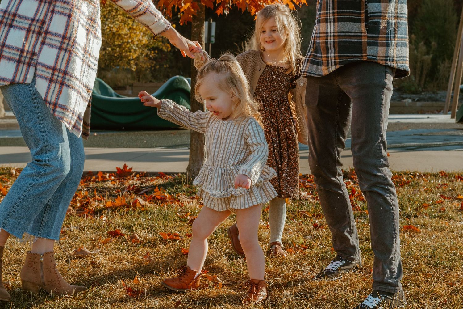 A family enjoys playing together in fallen autumn leaves during golden hour sunset in a park.