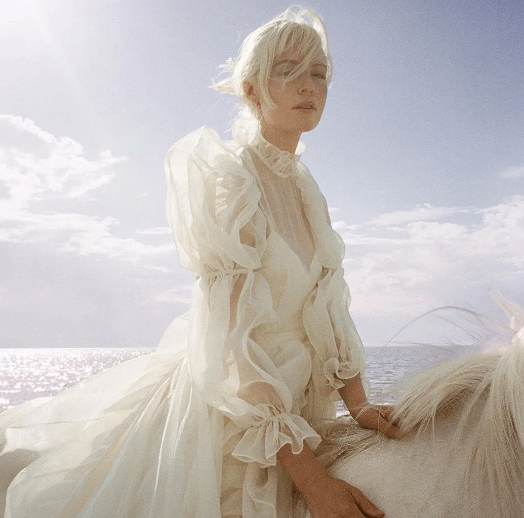 Ethereal outdoor portrait in flowing white dress against bright sky and ocean backdrop.