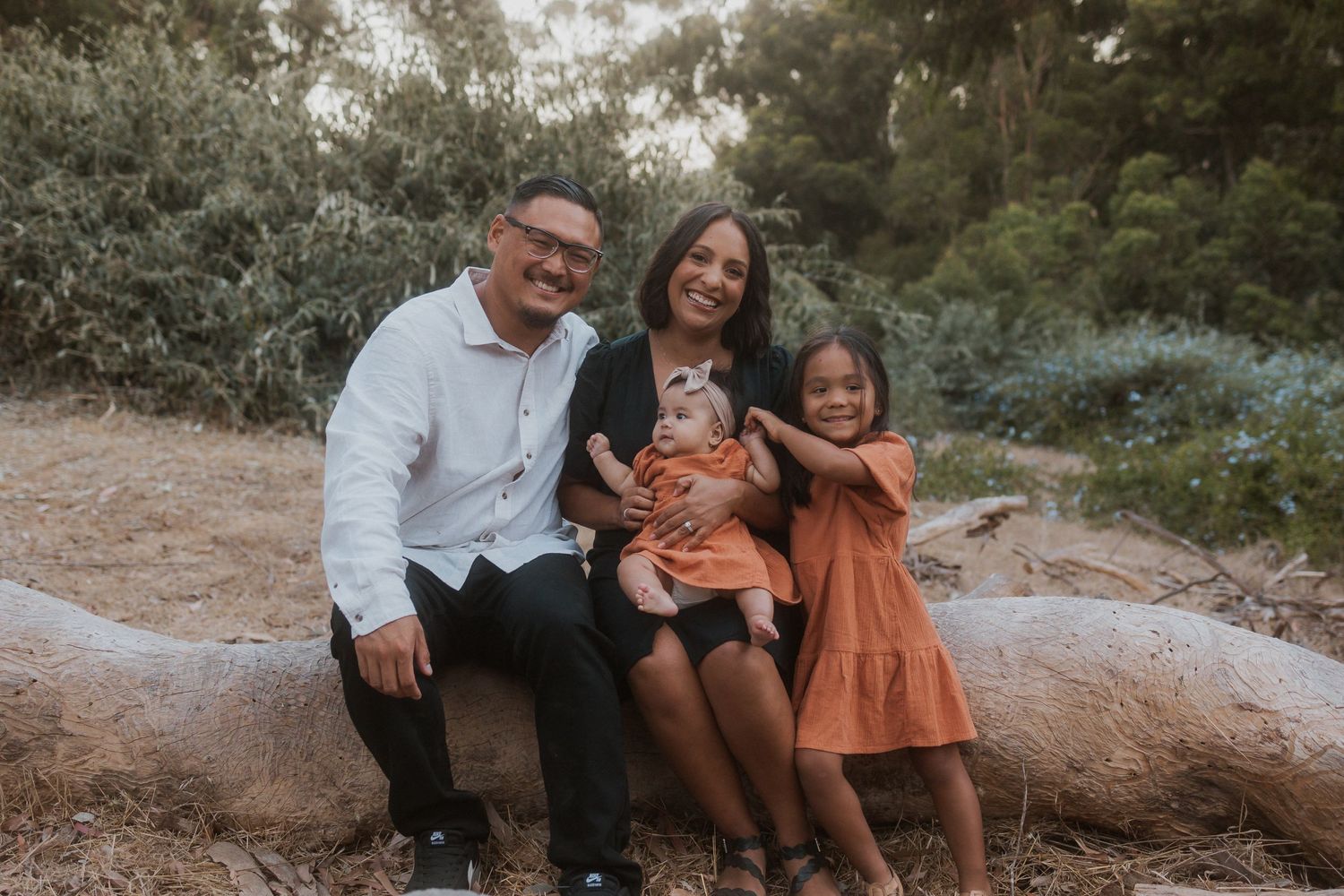 Happy family sitting together on rock during outdoor photo session.