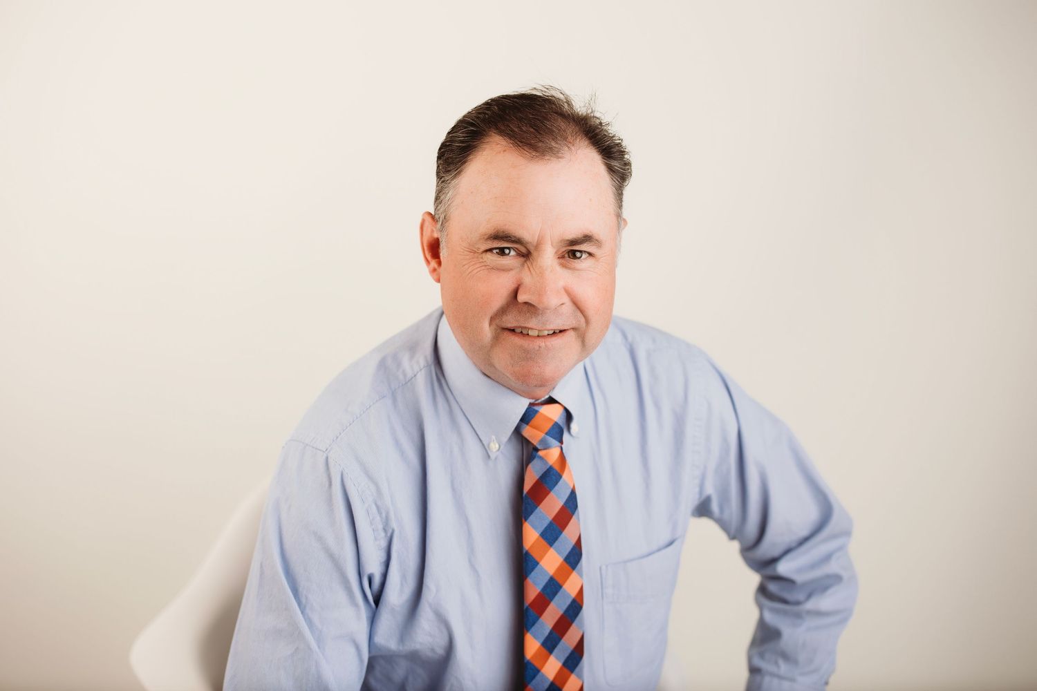Business casual portrait in light blue shirt and striped tie against white background.