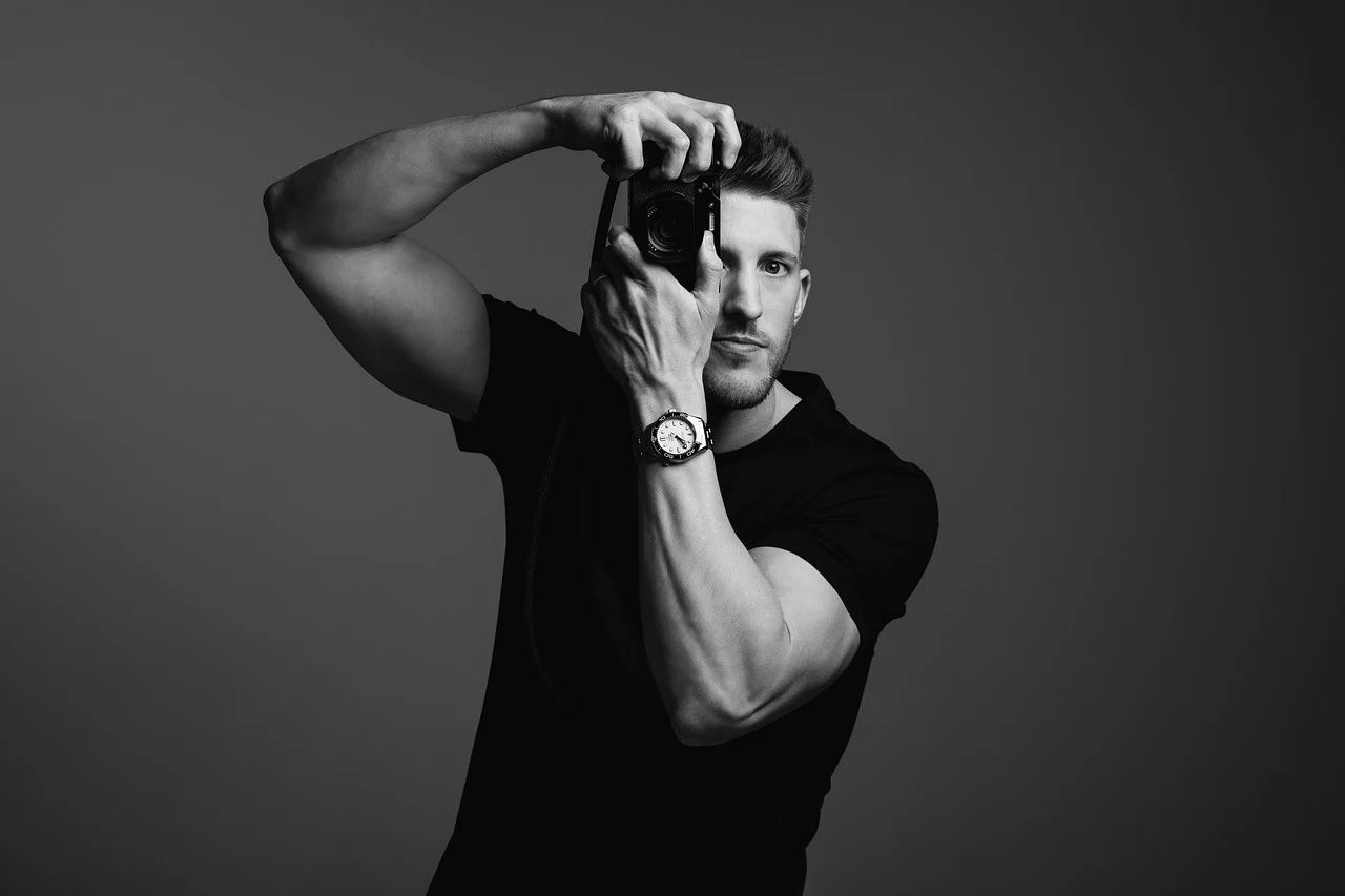 A person in a black sweater poses for a professional black and white portrait.