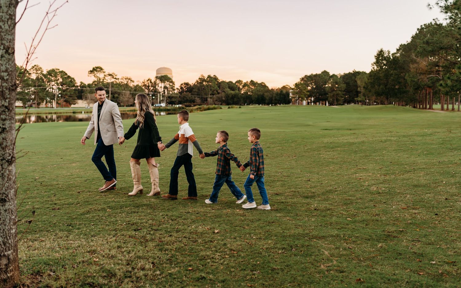 A group walks hand in hand across a grassy field at sunset with trees in the background.
