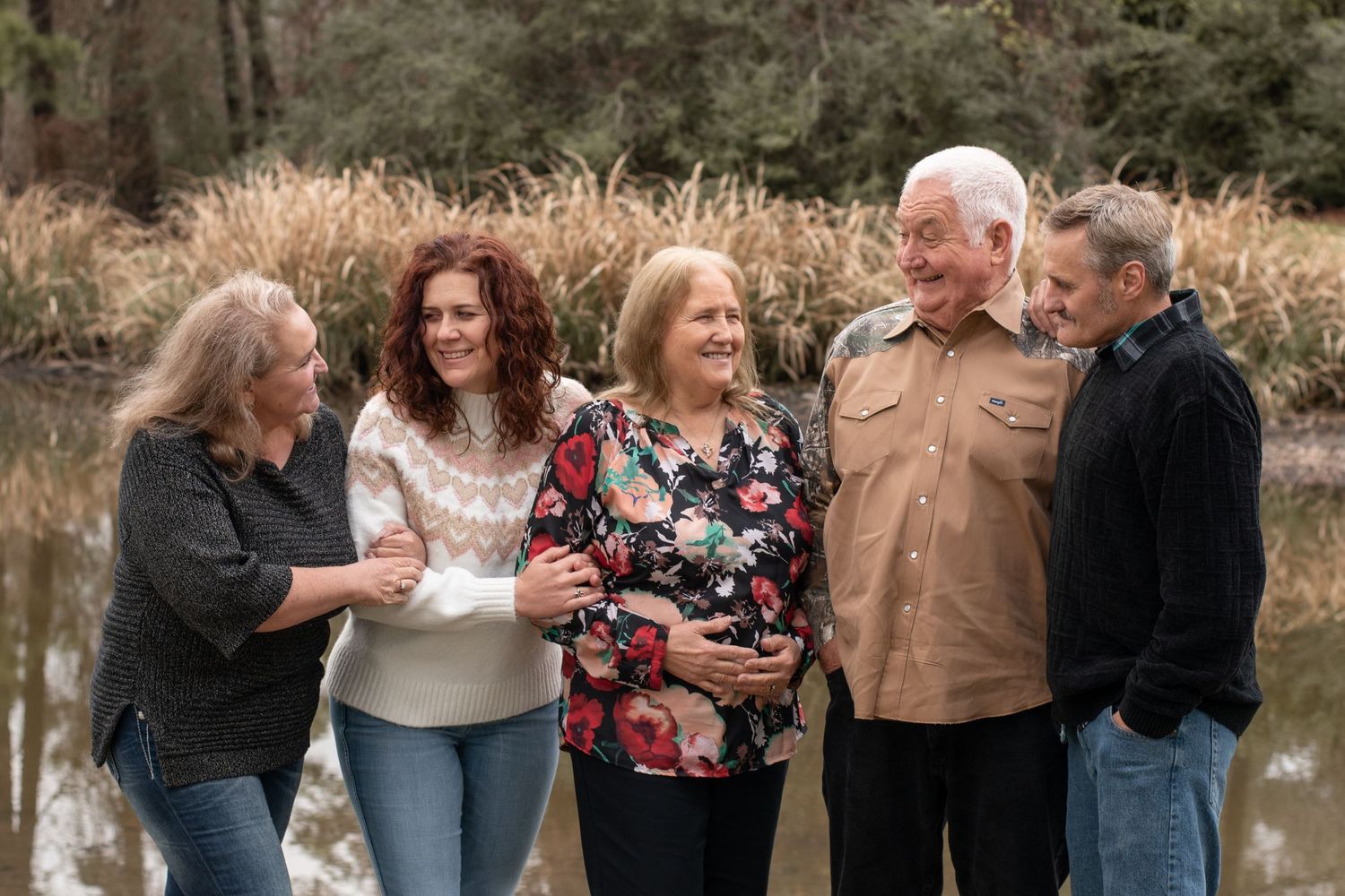Five people standing together laughing and enjoying a moment by a pond on an autumn day.