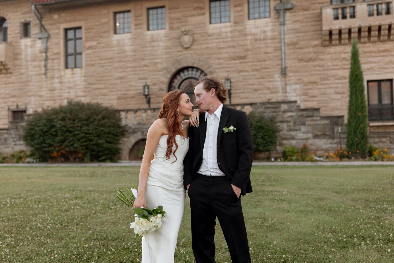 Wedding couple embraces on the lawn in front of a beautiful stone mansion.