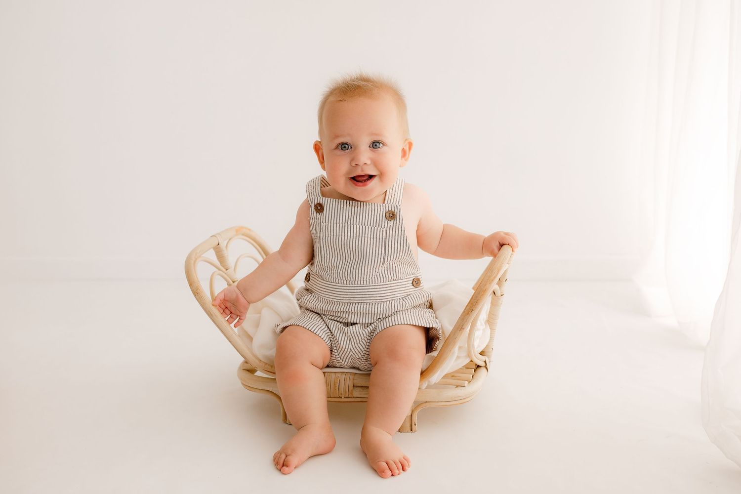 Baby milestone session with infant sitting in wooden prop against white backdrop.