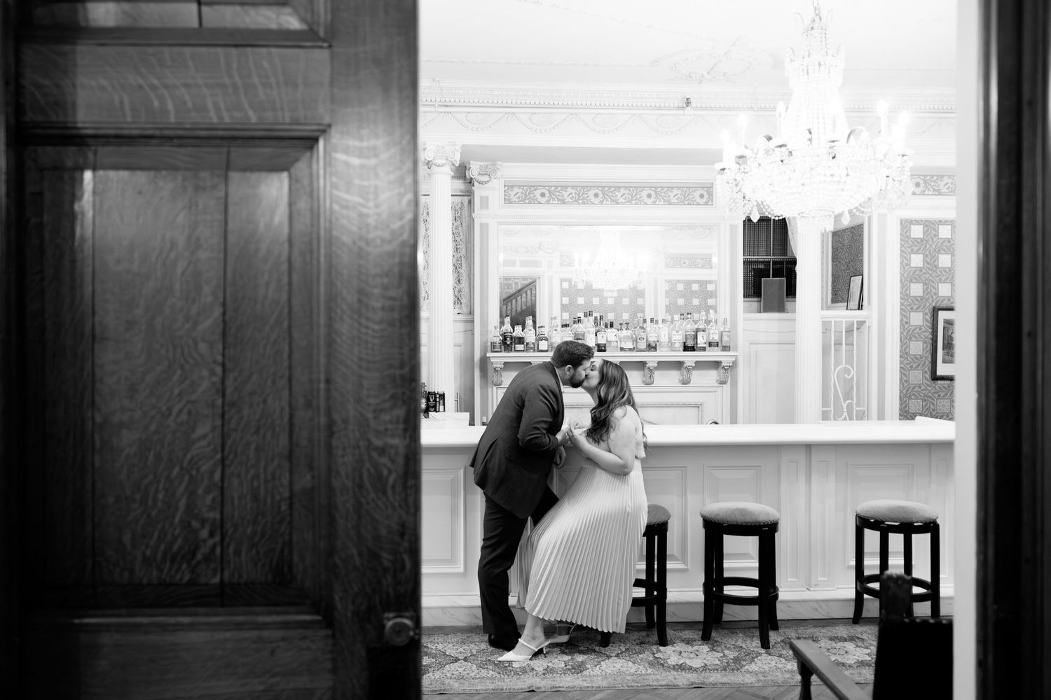 A black and white photograph shows two people in a vintage diner interior with wooden stools at a counter.