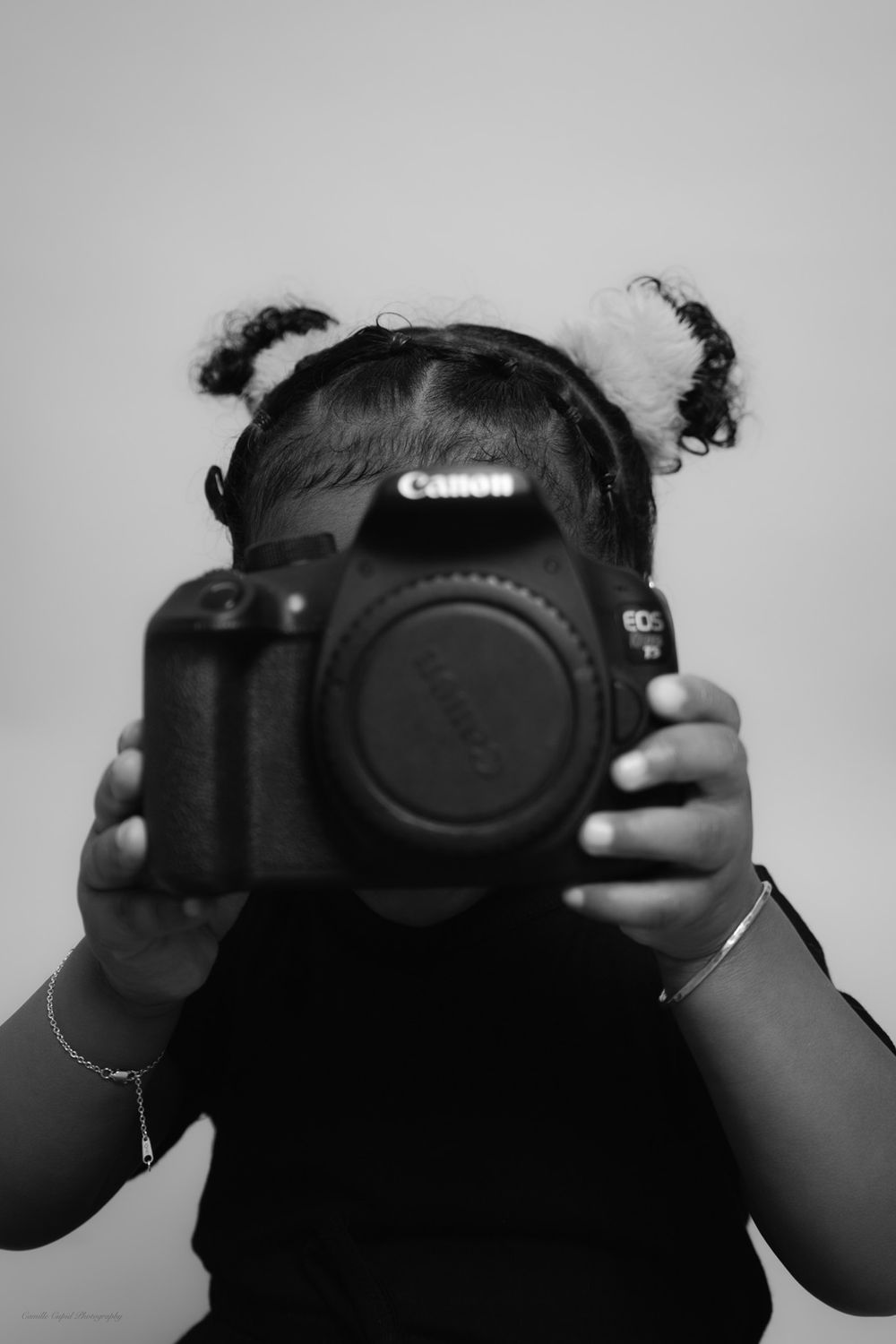 Black and white photo of hands holding a DSLR camera with the lens cap removed against a gray background. Pittsburgh Photographer. Cupid