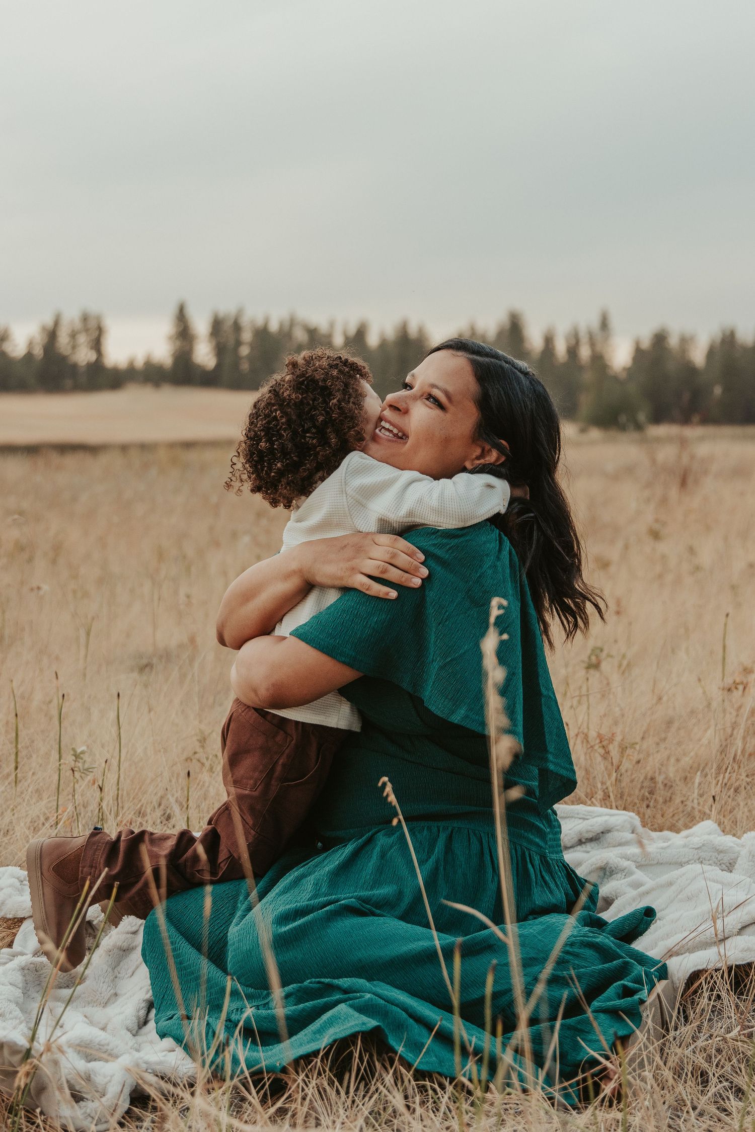 Expecting mother cradling her baby bump in a deep green maternity dress, surrounded by nature in Spokane