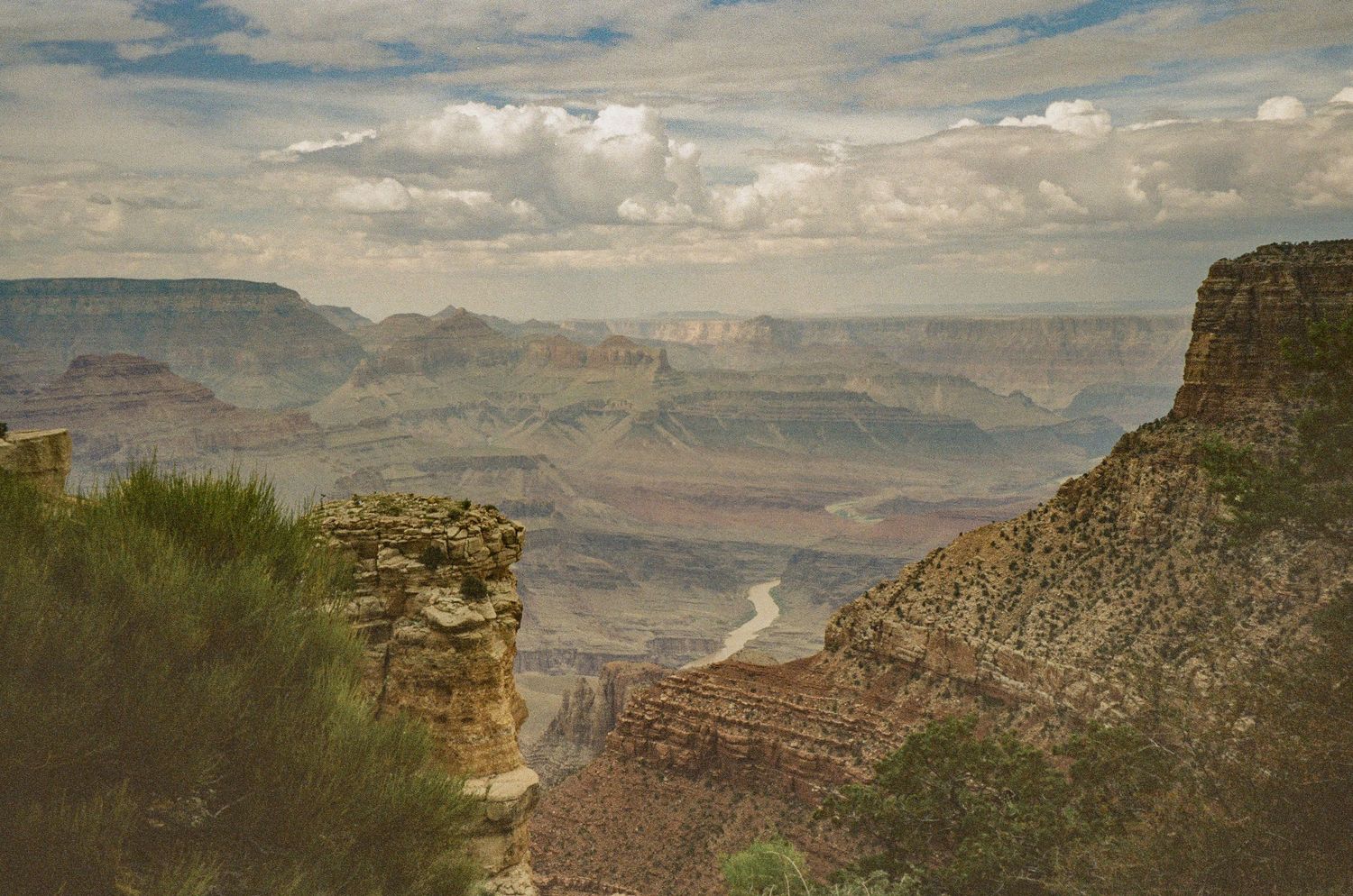 Sweeping vista of the Grand Canyon's red rock formations and deep valleys beneath puffy clouds.