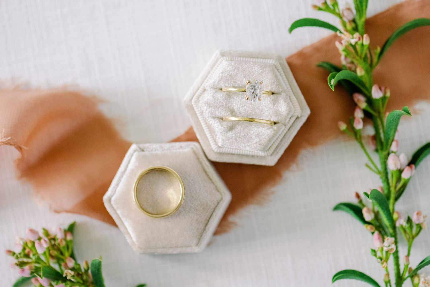 Two hexagonal ring boxes with greenery styled on a peach-colored surface.