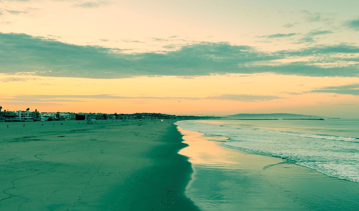 A serene beach at sunset with turquoise waves, golden sky, and a distant coastline stretching into the horizon.