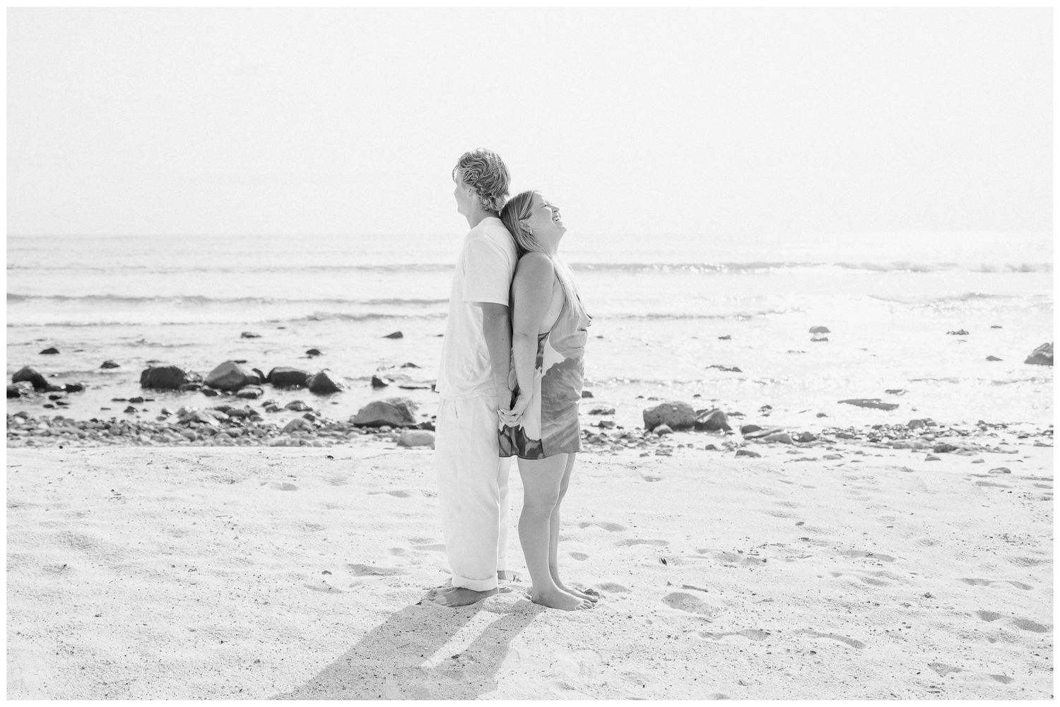 St. Regis Punta Mita Engagement Photographer documenting a couple embracing back-to-back on the sandy beach near the ocean shoreline.