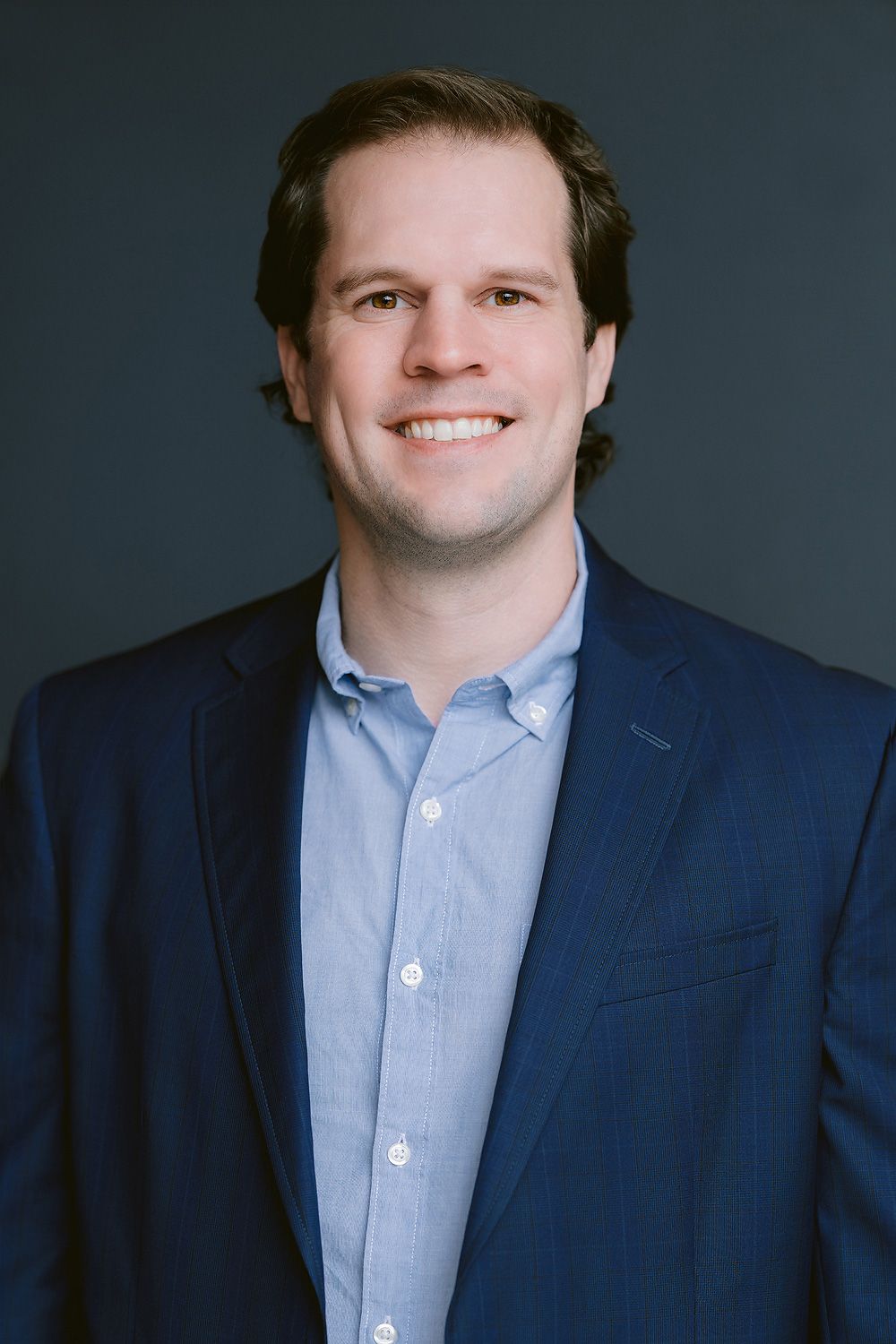 Young man with short hair and beard smiles for professional headshot in gray polo shirt.