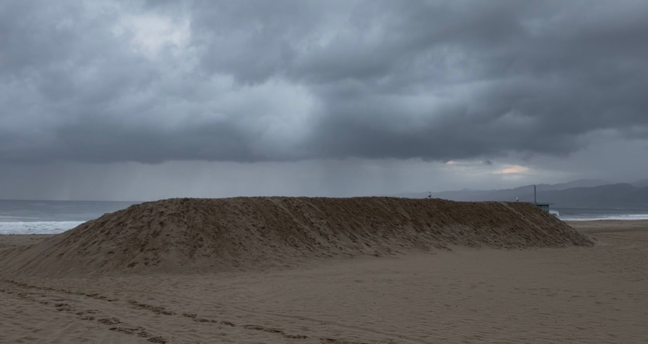 Large sand mound on a cloudy beach with stormy skies and ocean in the background.