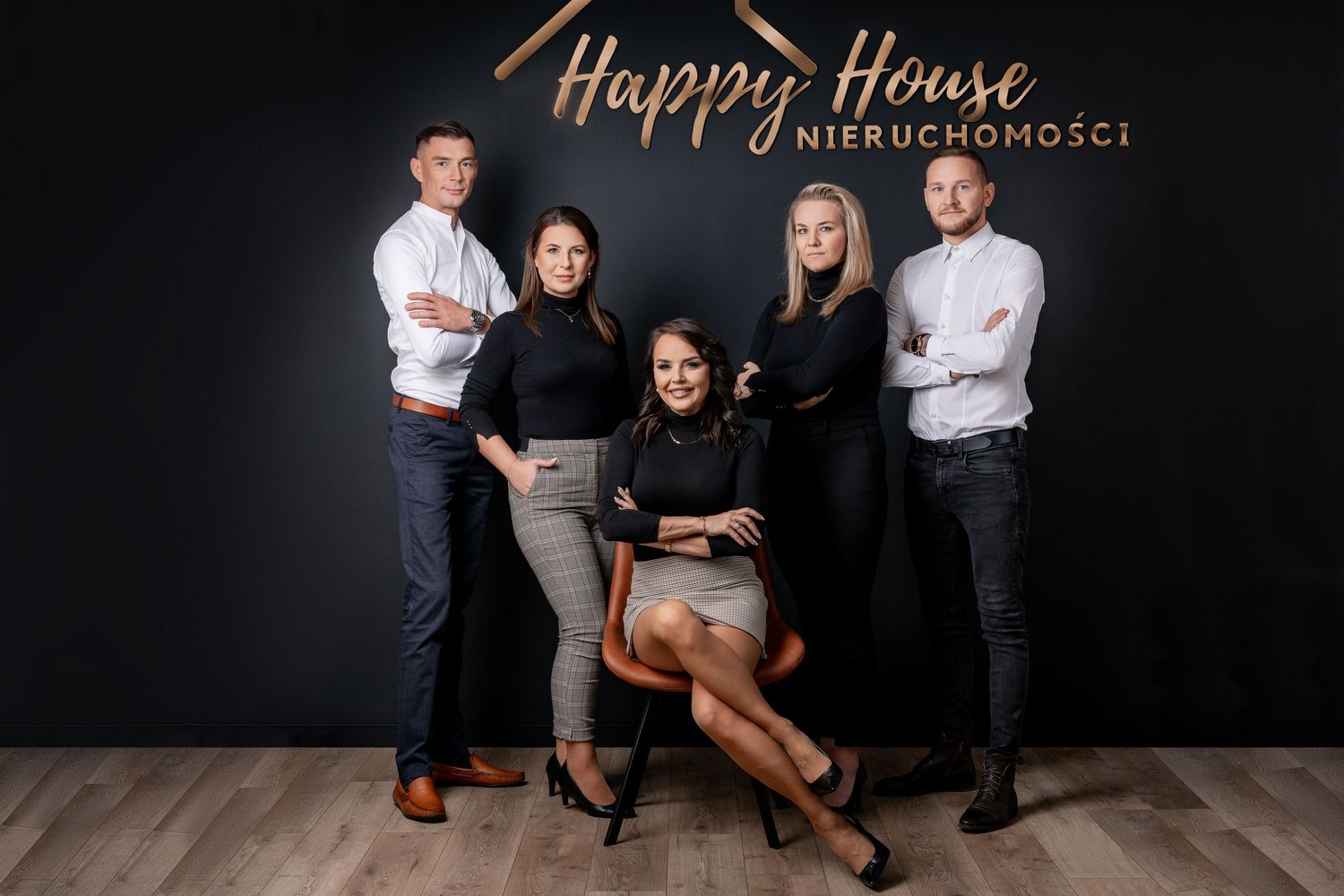 Real estate team members stand together in professional attire against dark wall with copper branding.