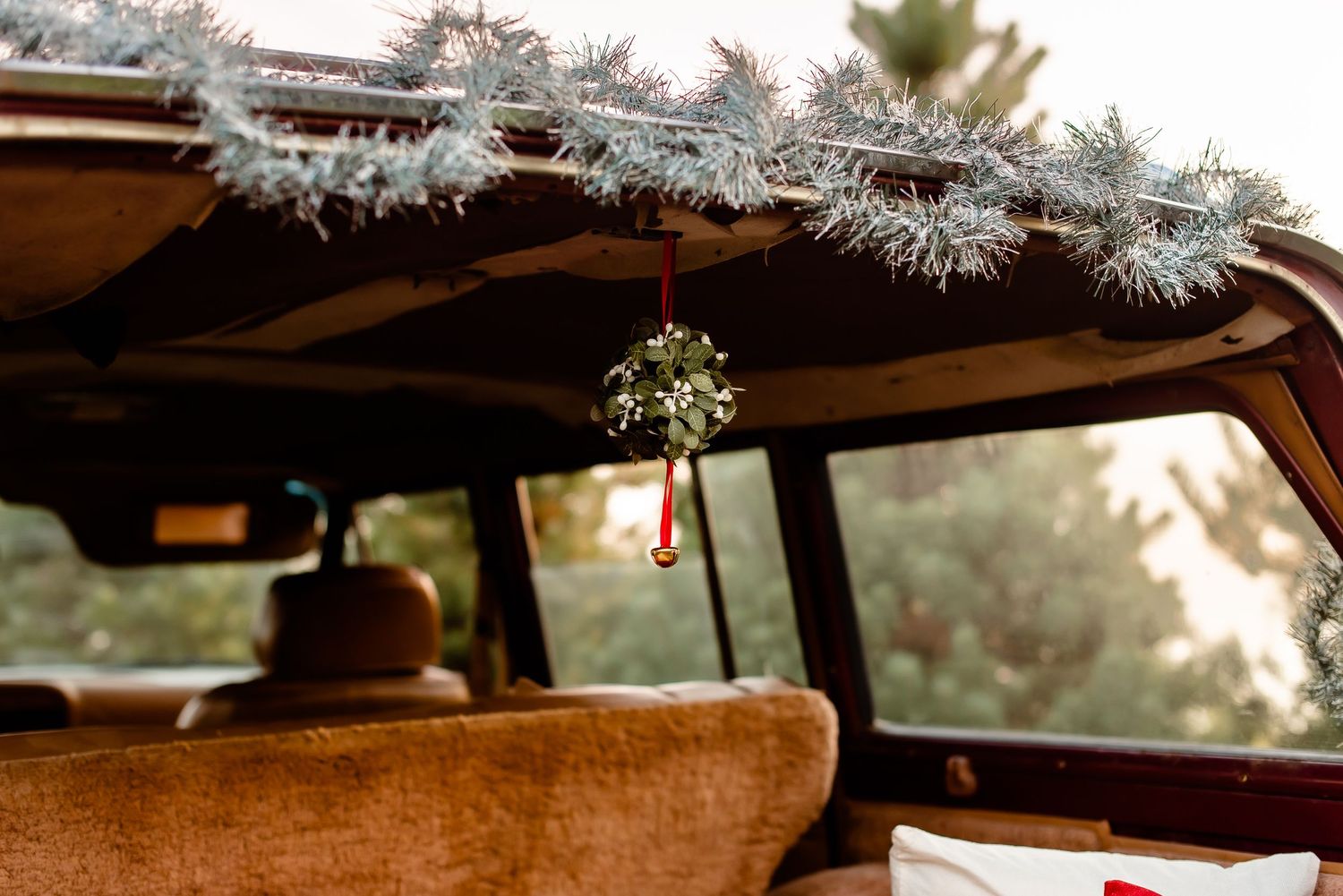 Silver tinsel and mistletoe decorations hanging from a vintage car's interior roof.