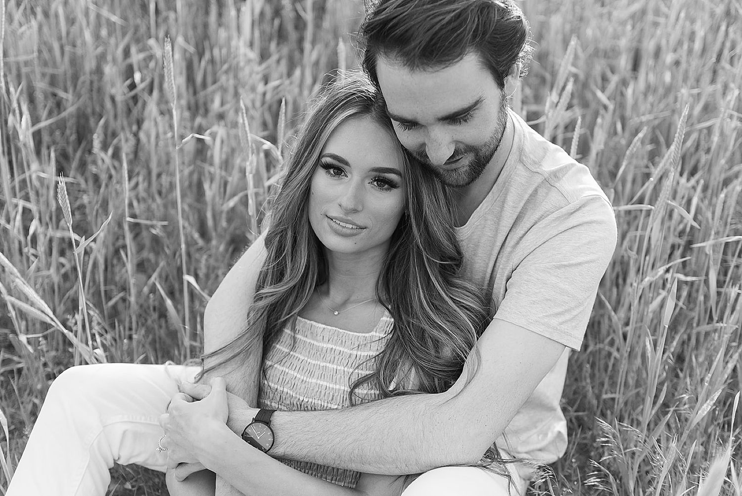 Intimate black and white portrait of couple sharing tender moment in tall grass.