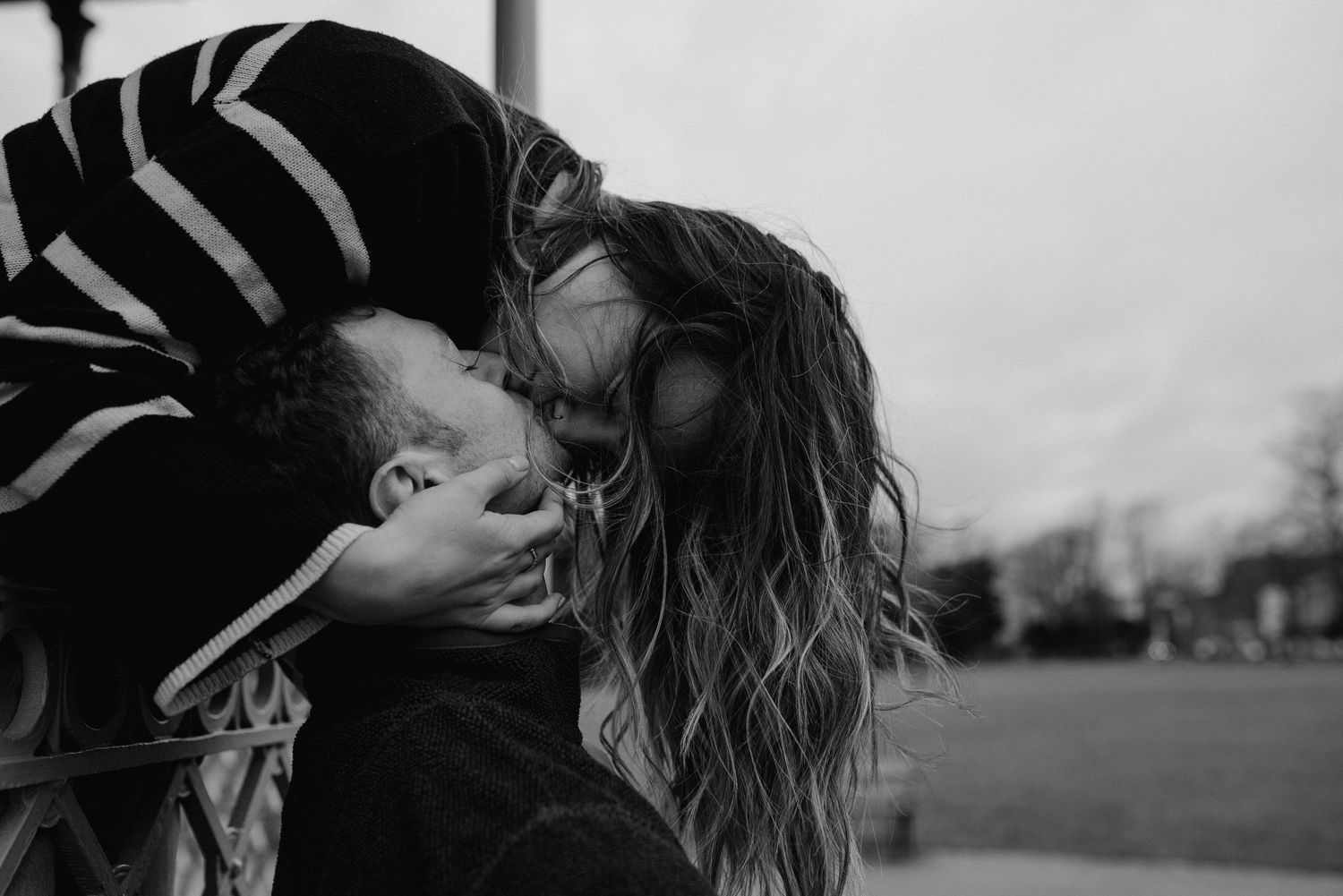 Intimate black and white portrait of couple in moody lighting by window.