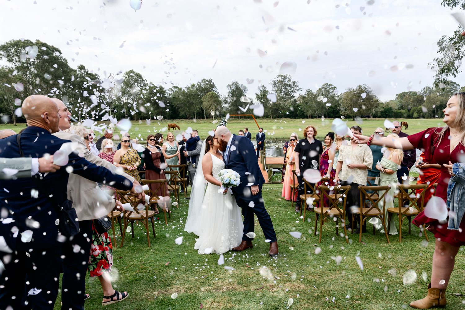 Wedding guests shower newlyweds with confetti on a grassy lawn during an outdoor celebration.