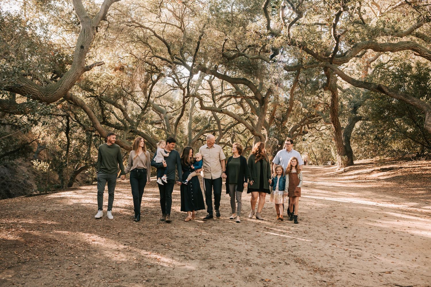 A romantic outdoor engagement session captures a couple in golden sunlight surrounded by lush trees in a park setting.