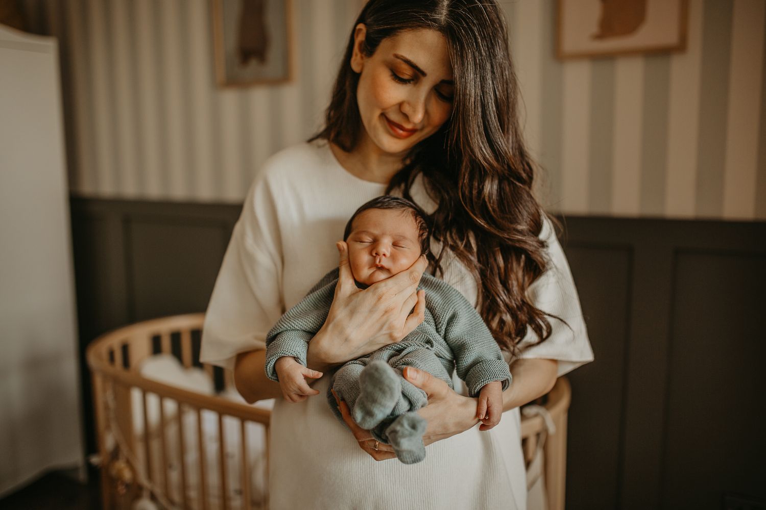 A baby in light blue sleepwear sleeps peacefully while being cradled in front of a wooden crib.
