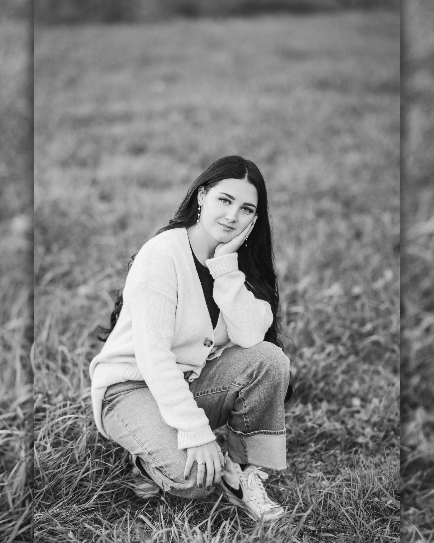 Person in white sweater and jeans sits casually on grassy field during outdoor portrait session.