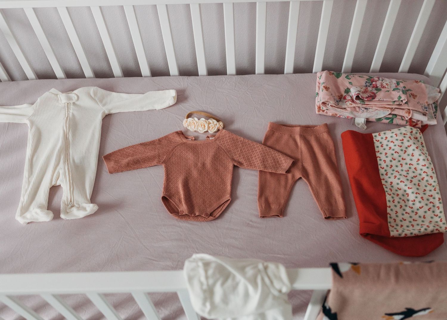Flatlay of baby clothing in neutral tones of white, beige and terracotta arranged neatly on a light background.