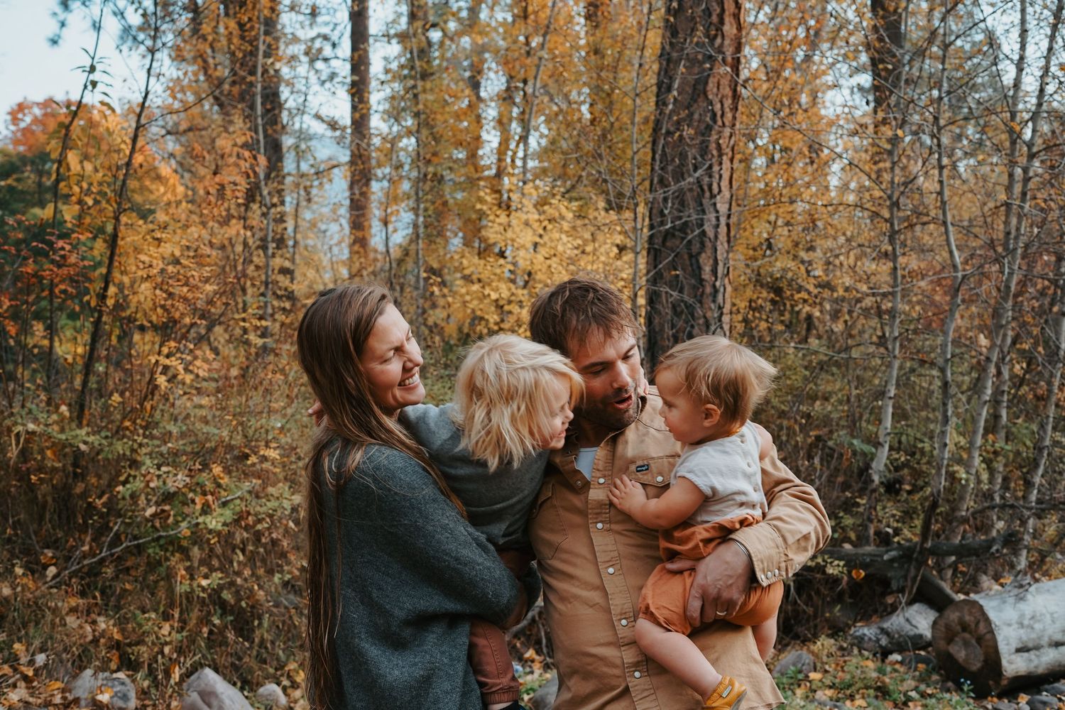 Family of four sharing a warm embrace in an autumn forest with golden foliage in the background.