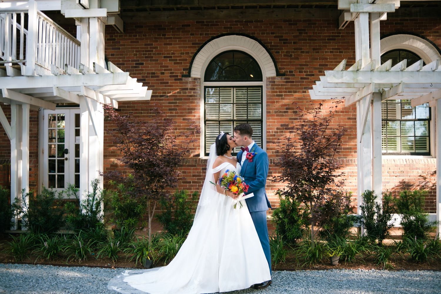 A romantic wedding couple shares an intimate moment in front of a beautiful brick mansion with white columns.