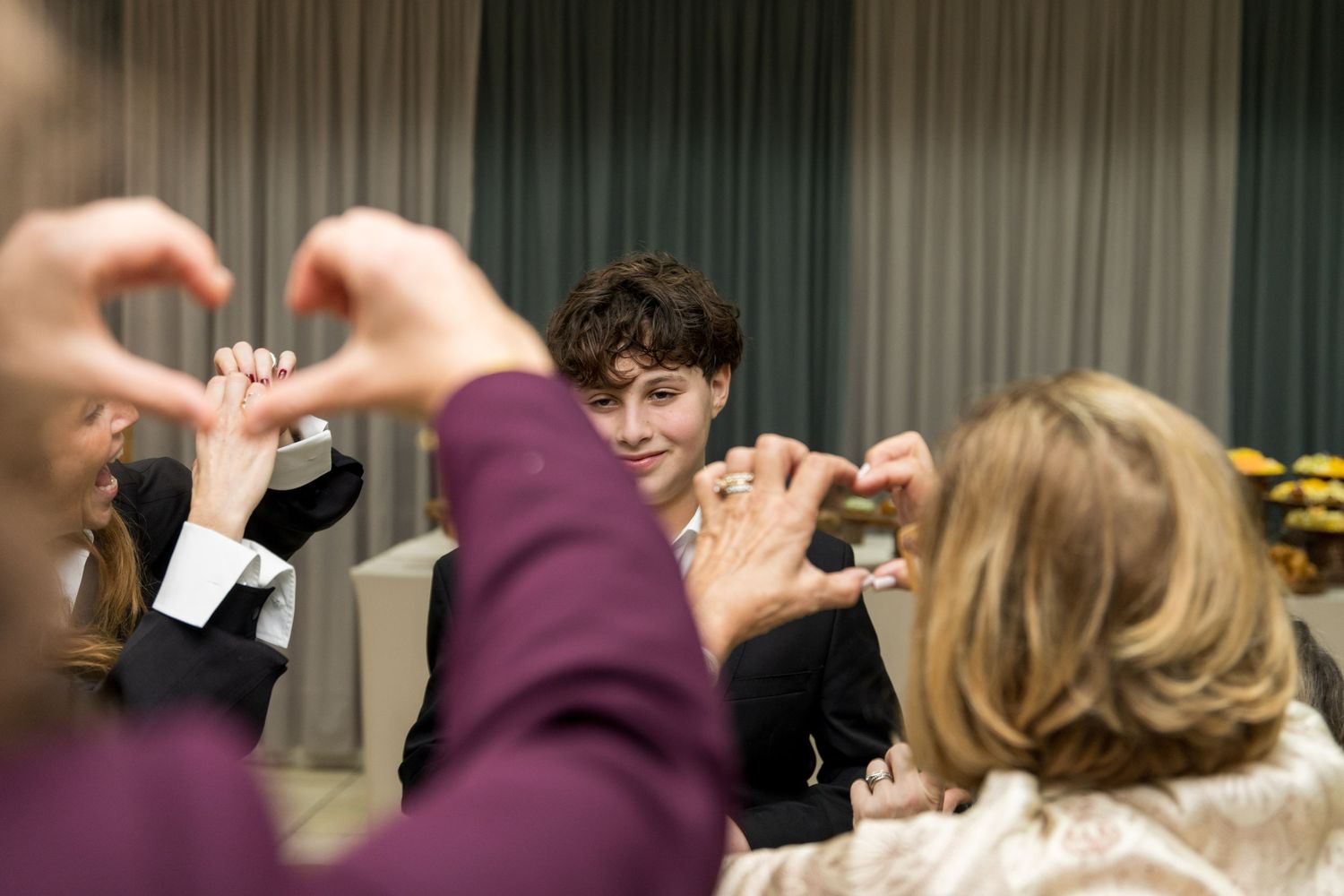 Un bar mitzvah regarde l'objectif et des invités au premier plan fond des cœurs avec leurs doigts