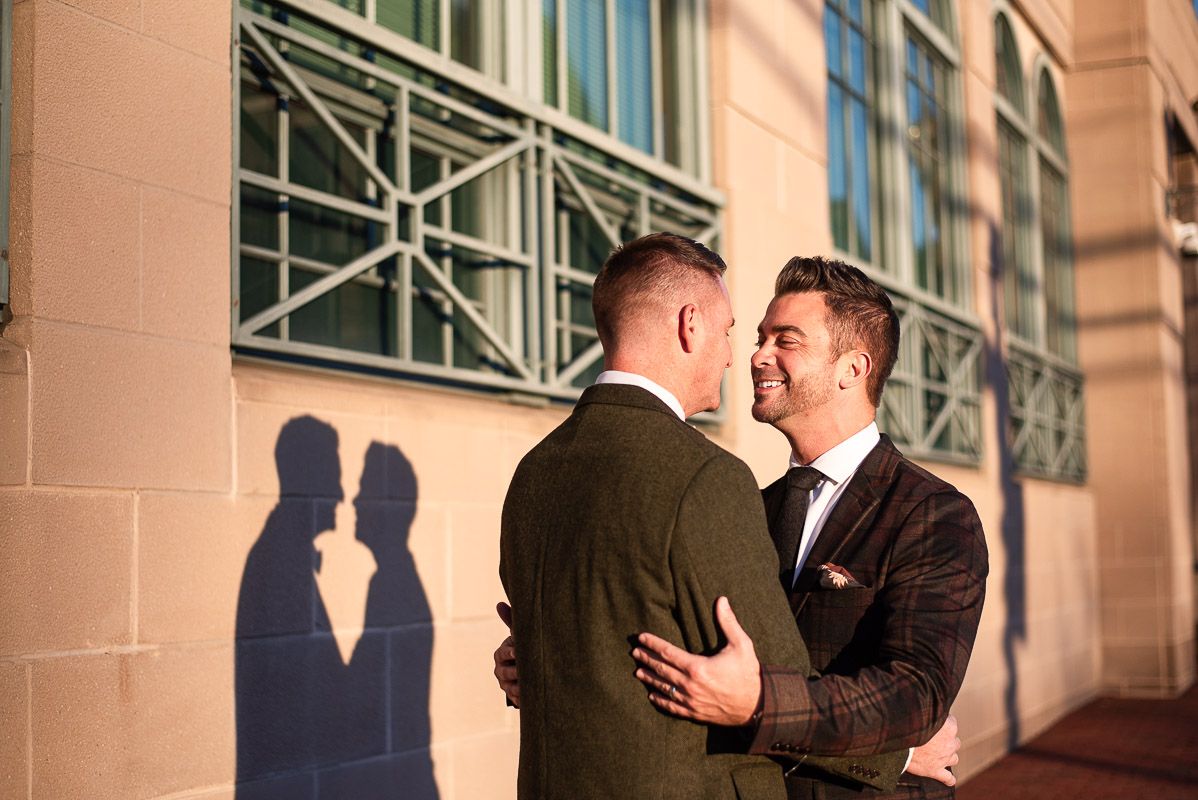 Two people in formal attire share an intimate moment in front of a stone building with ornate architecture.