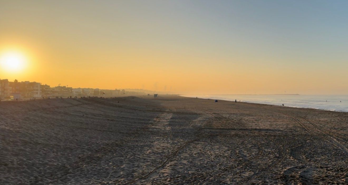 A panoramic view of a desert landscape at sunset with golden light illuminating the barren terrain and distant hills.
