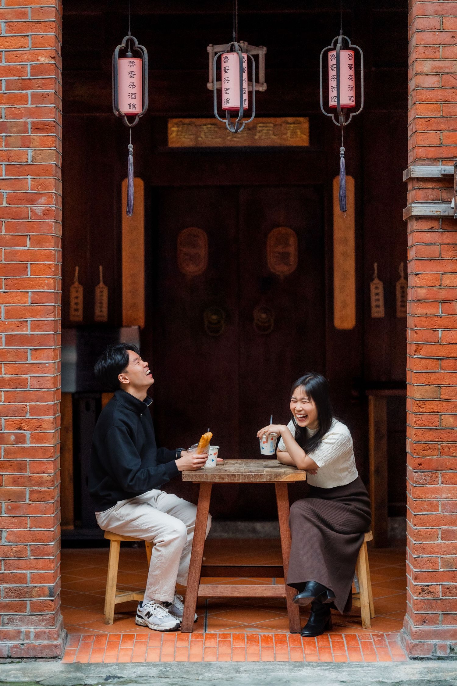 People sitting at a traditional Japanese style restaurant with brick walls and paper lanterns creating a cozy atmosphere.
