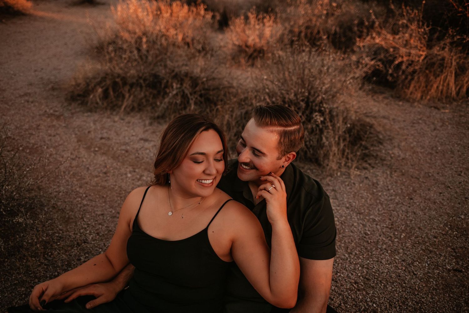 Alex and I sitting together on desert ground smiling at golden hour with warm brush background.