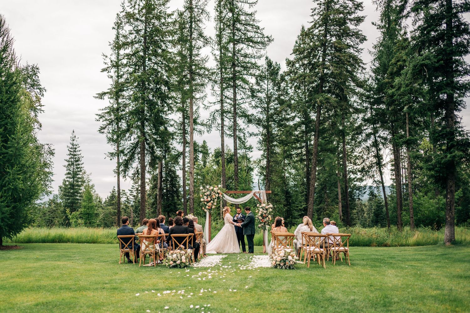 Outdoor wedding ceremony setup in a serene forest clearing with rustic wooden chairs and floral arrangements.
