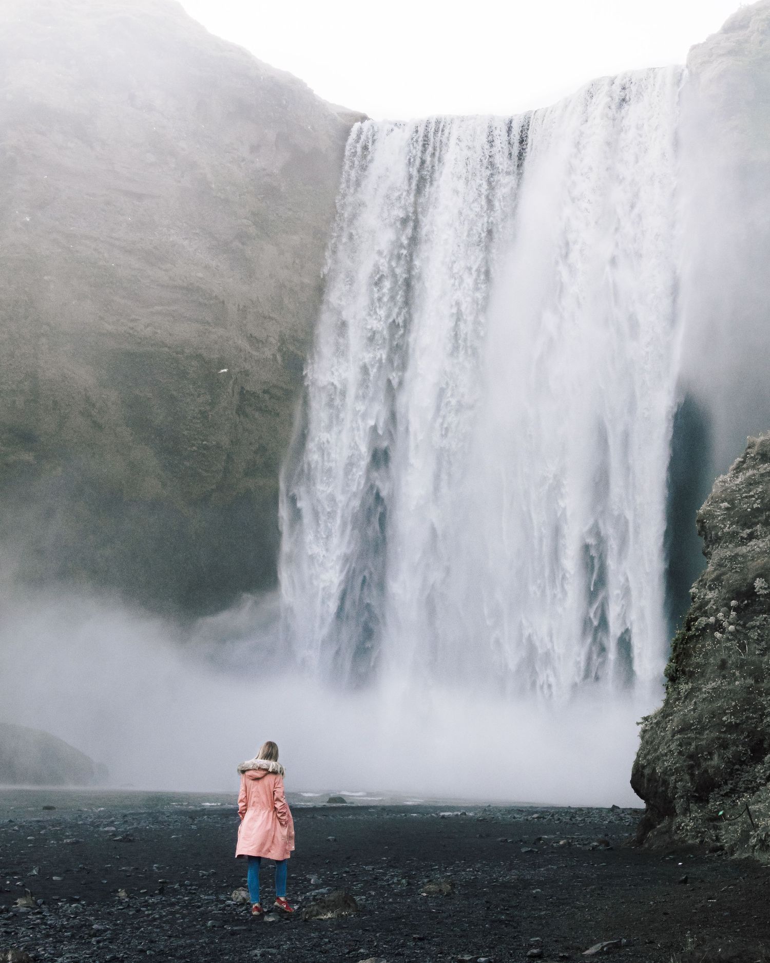 Majestic waterfall cascading down dark cliffs with misty spray in the foreground.