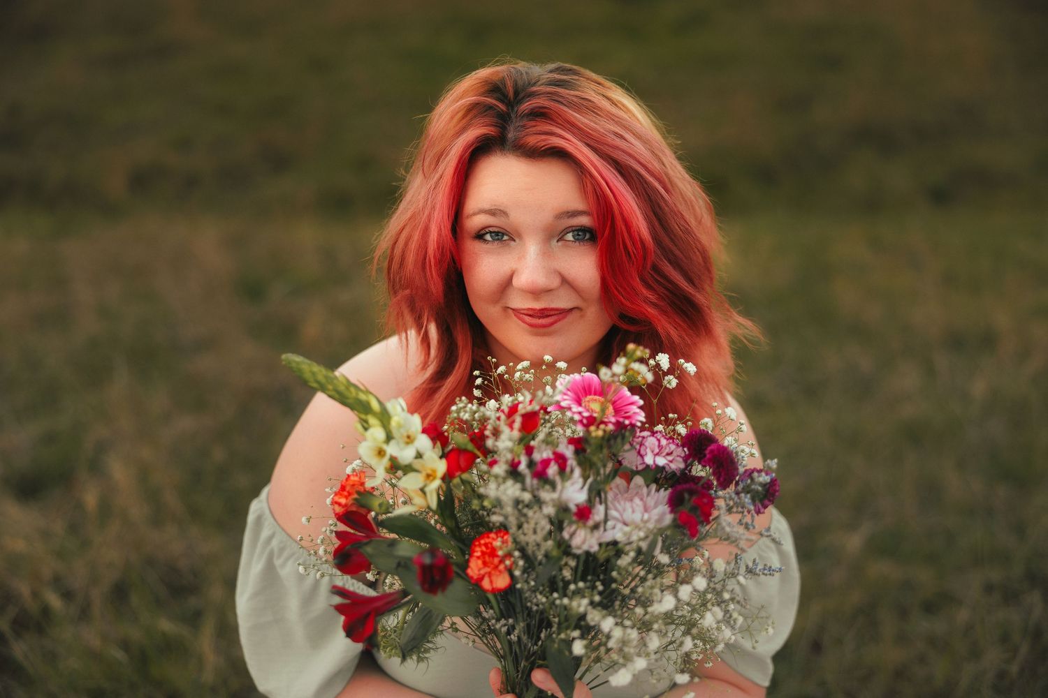 A person with vibrant red hair holds a colorful bouquet of flowers in an outdoor setting.