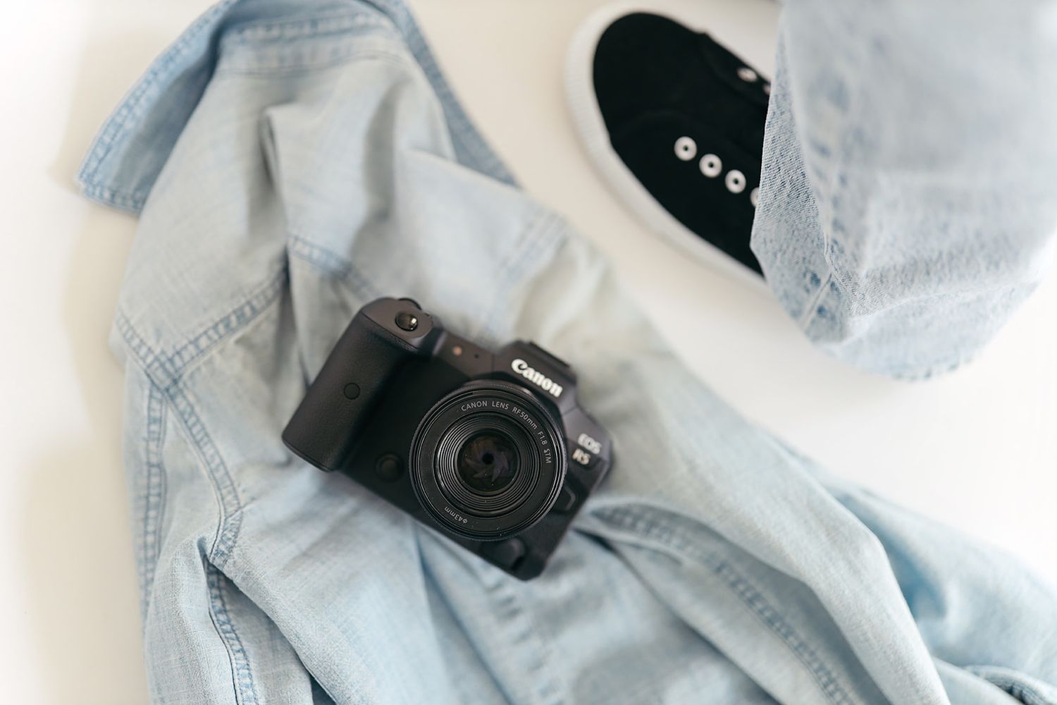 Arrangement of light denim clothing items and accessories including jeans, jackets, and camera on white background.