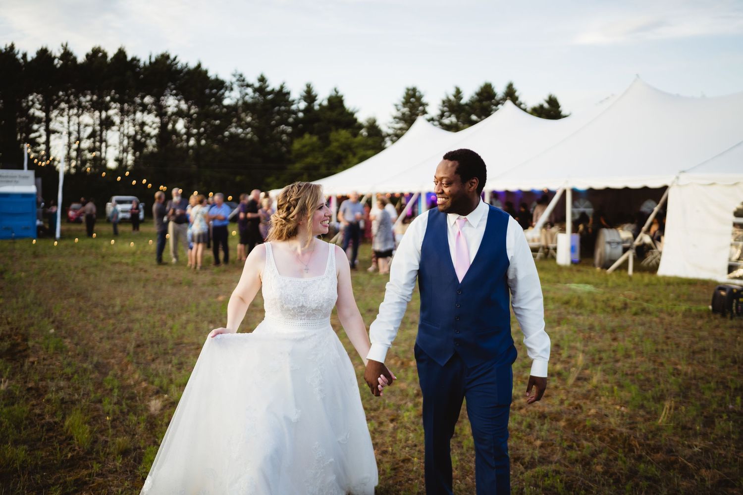 Newlywed couple walks through golden meadow at sunset creating romantic silhouettes against the sky.