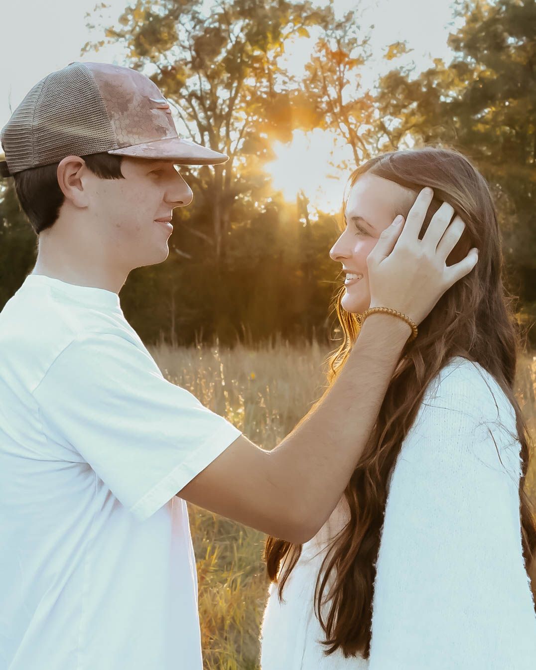 Romantic sunset photo of couple in white shirts standing in a golden field.