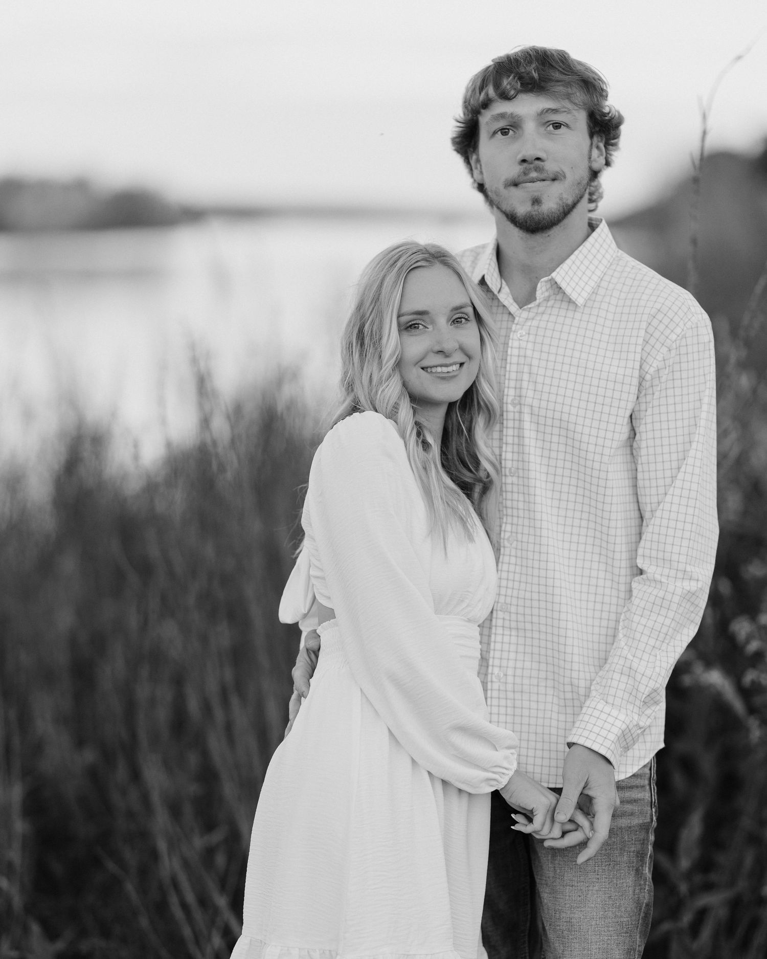 A couple embraces in a romantic outdoor photoshoot wearing white and plaid outfits in black and white style.