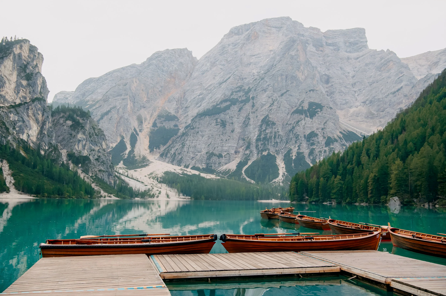 Scenic mountain lake surrounded by towering peaks with wooden boats docked along turquoise waters in the Dolomites.