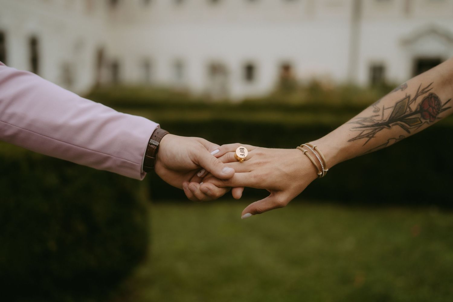 Close-up of hands with tattoos reaching towards each other outdoors.
