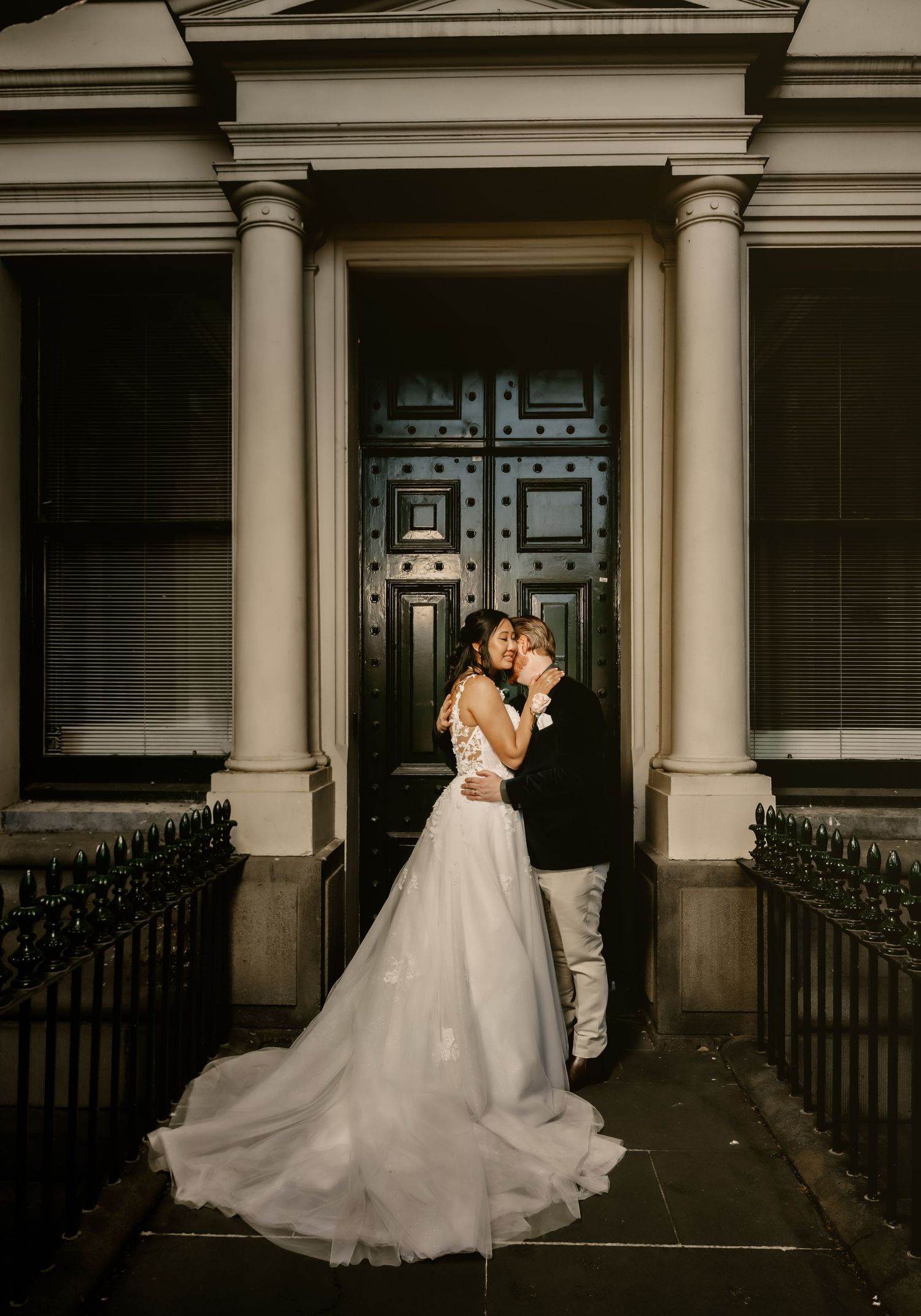 Newlywed couple shares romantic dance under ornate columns in dim evening lighting.
